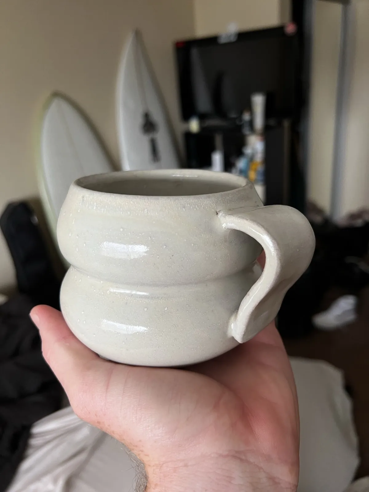 A white mug with a rounded double-bulb form, held in one hand