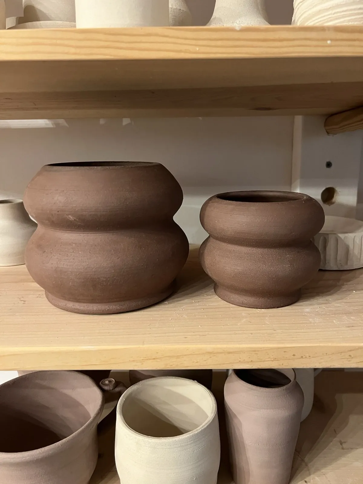 Two dark clay pots with stacked, rounded forms on a studio shelf