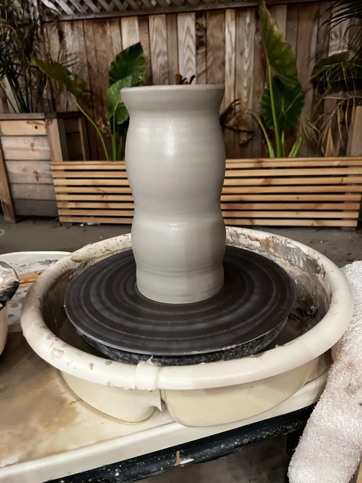 A freshly thrown white vase on the wheel