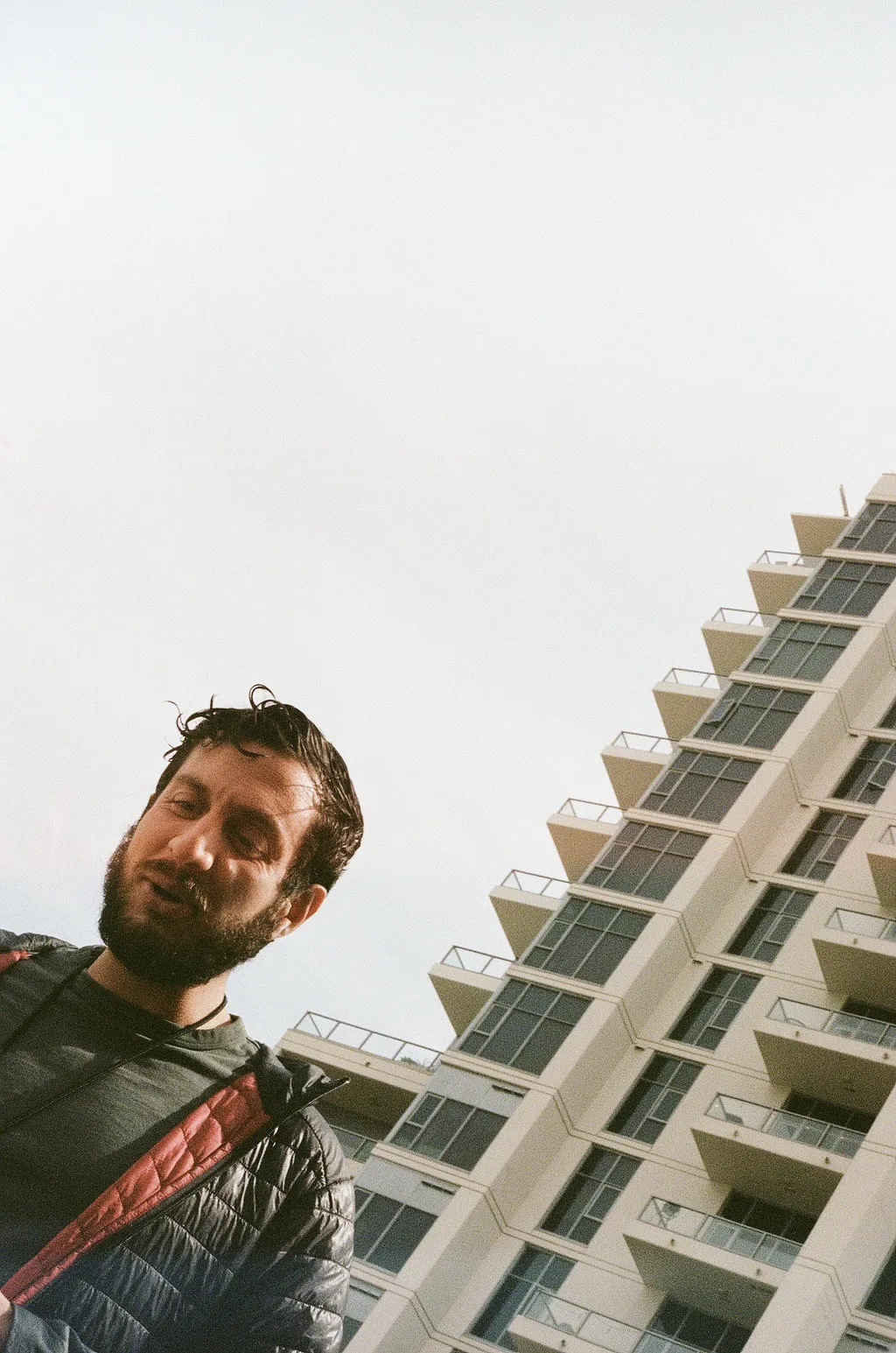 Self-portrait looking up beside a white high-rise