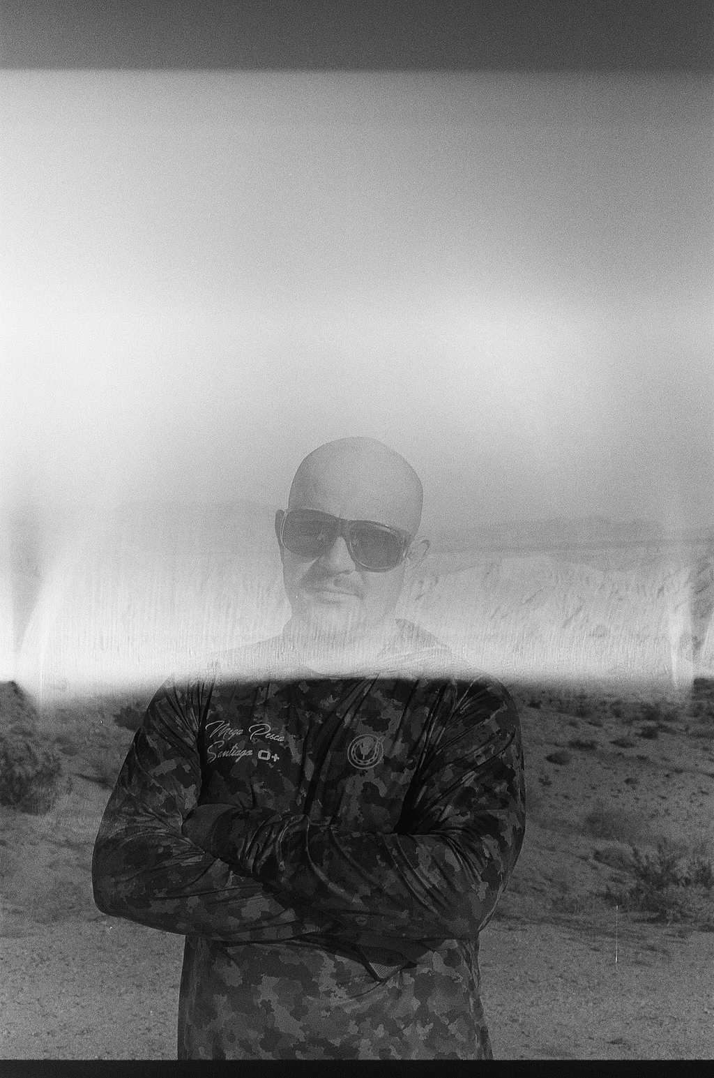 Black and white portrait of a man in sunglasses with arms crossed in the desert