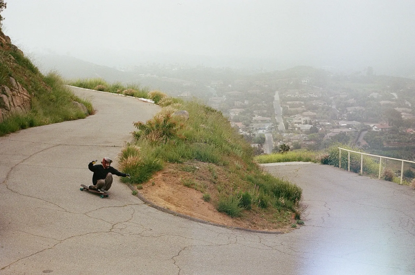 A skater leaning into a tight hairpin on a hillside road above the city