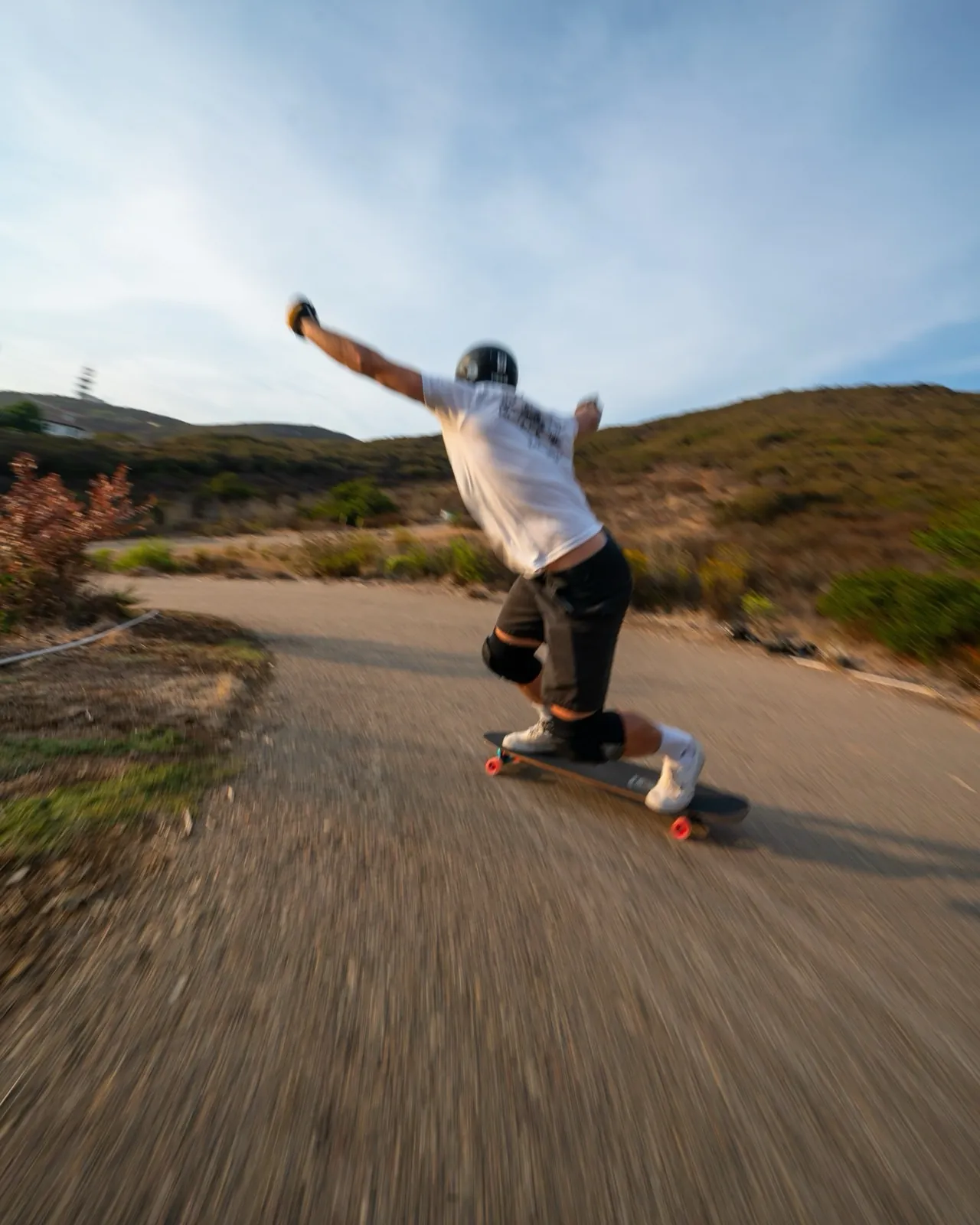 A skater crouched low with an arm out, carving a fast turn on a hill road