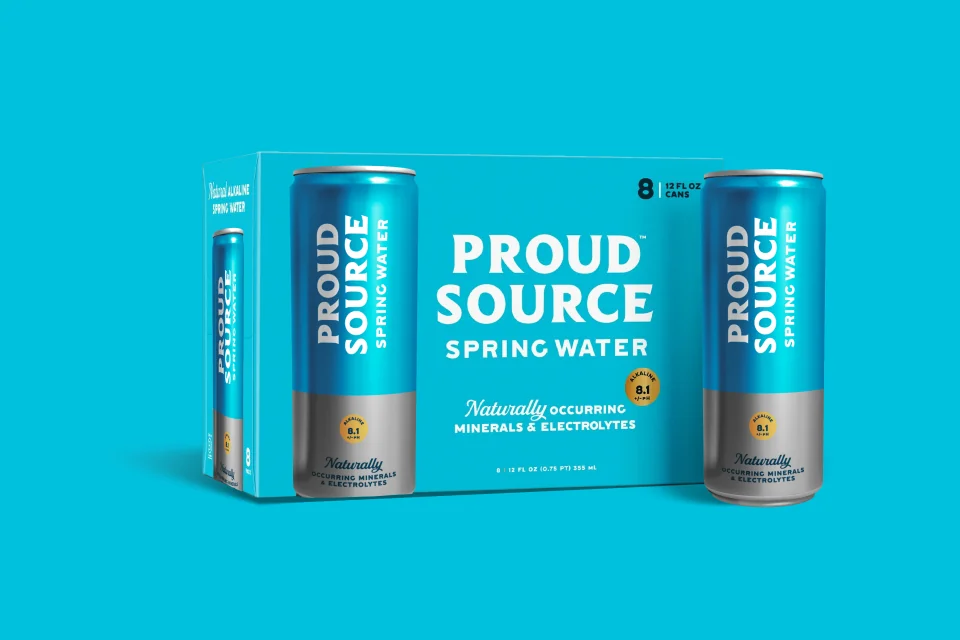 A Proud Source spring water can beside an eight-pack on a bright blue background